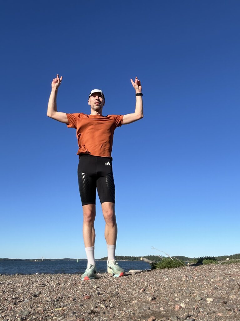 Juoksija kädet ylhäällä rannalla, sininen taivas